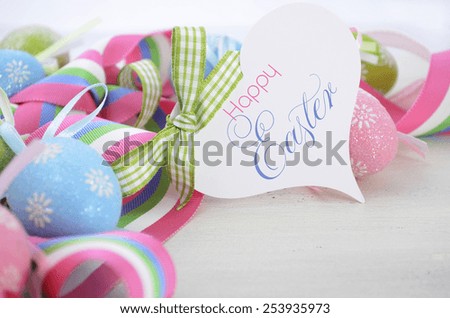 Happy Easter background with pink, blue and green ornament eggs and ribbon on vintage style rustic distressed white shabby chic wood table, with copy space for your text here, with greeting tag.