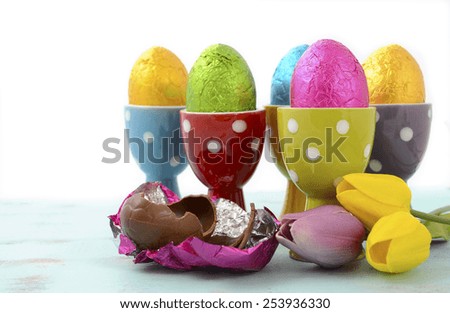 Happy Easter chocolate eggs wrapped in bright color foil in red, yellow, blue, green and purple polka dot egg cups.