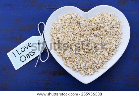 Plate of nutritious and healthy oat flakes in heart shaped bowl on dark blue rustic wood table, with I Love Oats message tag.