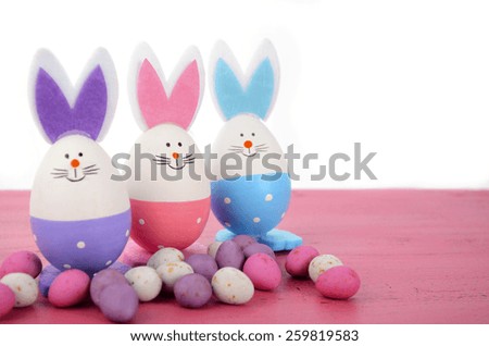Pink, purple and blue cute Easter eggs with bunny ears and faces on pink wood table