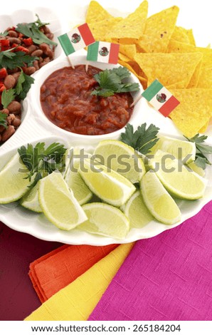 Happy Cinco de Mayo bright colorful party food with chilli beans, corn chips, salsa and limes platter on red wood distressed red table.