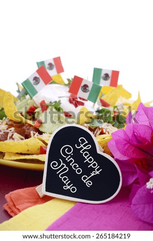 Happy Cinco de Mayo party table with nachos food platter and bright orange, red, and pink napkins on a red wood background.