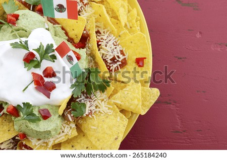 Happy Cinco de Mayo party table with nachos food platter and bright orange, red, and pink napkins on a red wood background.