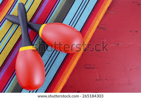 Happy Cinco de Mayo background with red and yellow maracas on Mexican style fabric and distressed red wood table.