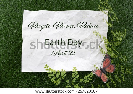 Earth Day, April 22, Concept with recycled paper in grass with fern and butterfly and text.