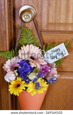 Happy May Day traditional gift of Spring flowers in orange cone hanging from door handle on wooden door.