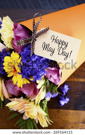 Happy May Day traditional gift of Spring Flowers in orange paper cone on dark wood table.