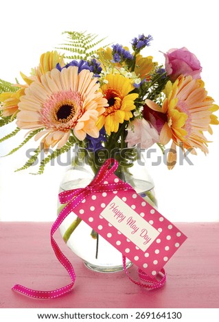 Happy May Day gift of Spring flowers in vase with greeting tag on pink wood table.