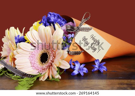 Happy May Day traditional gift of Spring Flowers in orange paper cone on dark wood table.