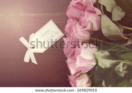 Mothers Day pink roses on rustic dark wood table with greeting gift tag, with applied vintage style filters and added light stream.