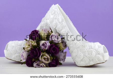 Wedding theme white floral bridal shoes with flowers on shabby chic white table and purple background.