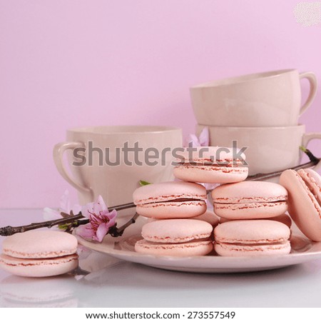 Plate of pink macaron cookies with vintage cups and plates on pink and white background.