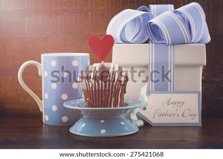 Happy Fathers Concept with blue and white gift, blue coffee mug, and cupcake on dark wood rustic background, with applied retro filters and lens flare sun beam.