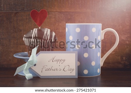 Happy Fathers Gift with cupcake and  blue and white polka dot coffee mug on wood background, with applied retro filters and lens flare sun beam.