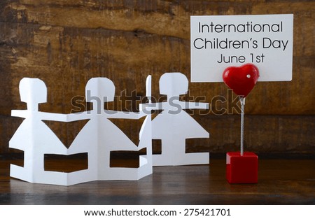 International Childrens Day concept with paper dolls on dark wood background, with message on red heart sign.