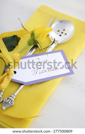 Yellow and white theme wedding table place setting with antique silverware, napkin and yellow rose bud on white shabby chic table