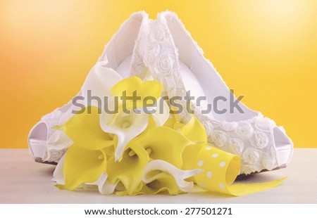 Yellow and white theme floral wedding bridal high heel shoes with calla lilly bouquet on shabby chic white wood table and yellow background, with added filters and lens flare.