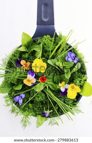 Cooking with herbs concept with fresh herbs and edible flowers in modern yellow fry pan skillet on white wood table.