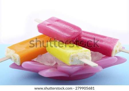 Summer is Here concept with bright color ice pop, ice creams on ice in pretty pink bowl blue background.