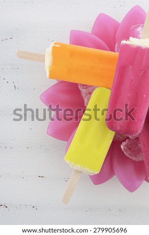 Summer is Here concept with bright color ice pop, ice creams on ice in pink flower bowl on white vintage wood table.
