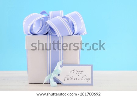 Happy Fathers Day Gift with Blue and White Ribbon with gift tag on white wood table and pale aqua blue background.