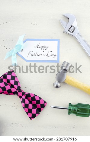 Happy Fathers Day concept with mens tools and pink bow tie and greeting card on white wood table.