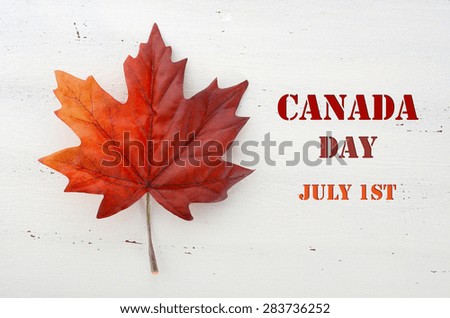 Happy Canada Day red silk maple leaf  on white wood shabby chic table with Canada Day, July 1st, text greeting.