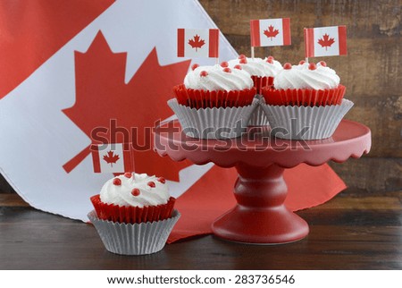 Happy Canada Day celebration cupcakes on red cake stand with red and white maple leaf flag against a rustic distressed wood background.