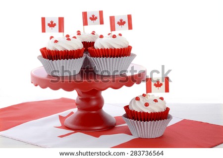 Happy Canada Day celebration cupcakes with red and white maple leaf flag on red cake stand against a white background.