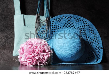 Ladies vintage retro style apparel with aqua blue sun hat, shoulder bag and necklace with bunch of pink hydrangea flowers against a dramatic black slate background.