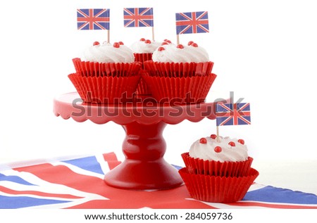 Red white and blue theme cupcakes on red cake stand with UK Union Jack flags on white wood table for Queens Birthday and Great Britain party food.