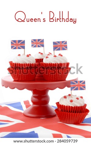 Red white and blue theme cupcakes on red cake stand with UK Union Jack flags on white wood table with Queens Birthday sample text.