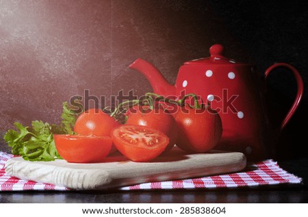 Kitchen still life with tomatoes, chopping board, polka dot tea pot on red check napkin against a black slate kitchen bench top, with applied filters and added light stream lens flare.