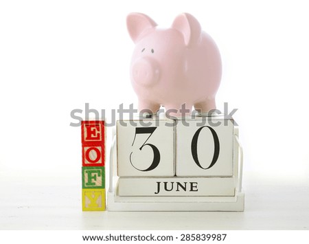 End of Financial Year Savings Concept with piggy bank, EOFY  building blocks and wood calendar on white wood table.