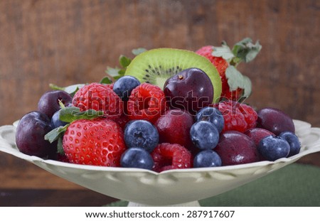 Summer Fruit including raspberries, strawberries, cherries, blueberries and kiwi fruit in a vintage bowl with reclaimed dark wood background.