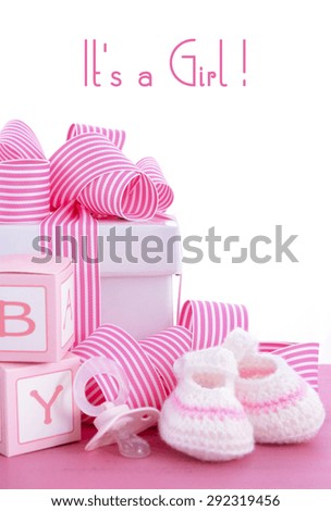 Baby shower Its a Girl pink gift with baby booties, dummy and gift box on pink shabby chic wood table.