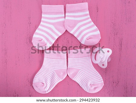 Its a Girl Baby Shower or Nursery concept with socks and pacifier dummy on pink shabby chic  wood
