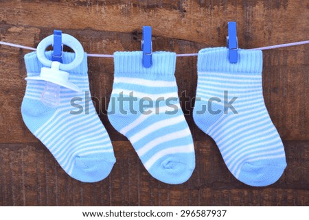 Its a Boy Blue Baby Socks and dummy pacifier hanging from pegs on a line against rustic dark wood background.