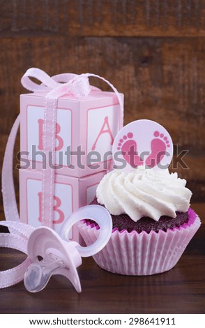 Its a Girl pink baby shower cupcake and gift box on vintage dark wood table background.