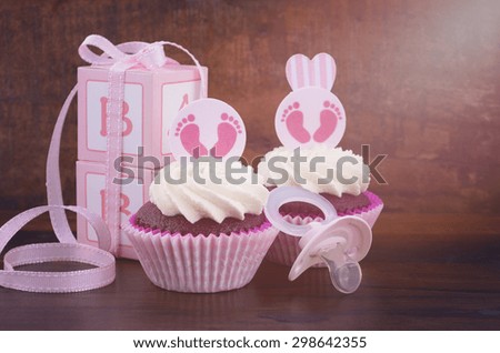 Its a Girl pink baby shower cupcake and gift box on vintage dark wood table background, with applied vintage style filters and lens flare.