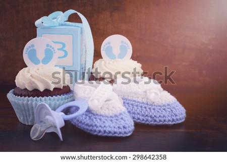 Its a Boy blue baby shower cupcake and gift box on vintage dark wood table background, with applied vintage style filters and lens flare.