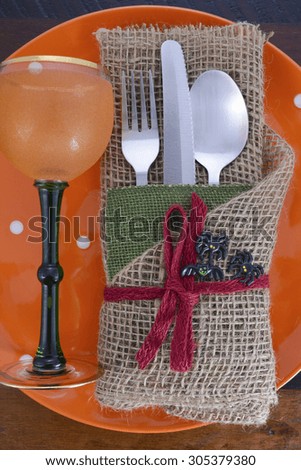 Rustic Halloween table place setting with burlap wrapped cutlery and orange plate and wine goblet on dark wood table