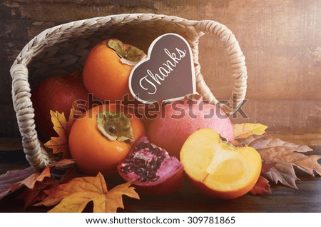 Thanksgiving Autumn feast fruit, with persimmons and pomegranates tumbling out of a basket with Thanks message on a rustic wood background, and added filters and lens flare light stream.