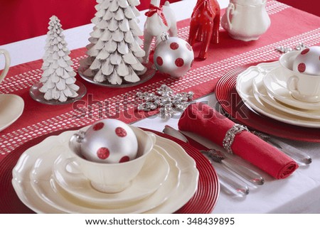 Festive red and white Christmas Table Setting with fine china place setting, reindeers and holiday ornaments and decorations, closeup.