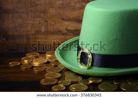 Happy St Patricks Day green leprechaun hat with gold covered chocolate coins on dark wood background.