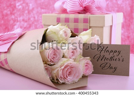 Happy Mothers Day gifts of pink roses and gift box wrapped in brown kraft paper on pink wood table, and greeting gift tag card.