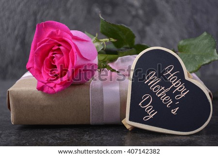 Mothers Day gift with pink rose and greeting on black slate background, closeup.