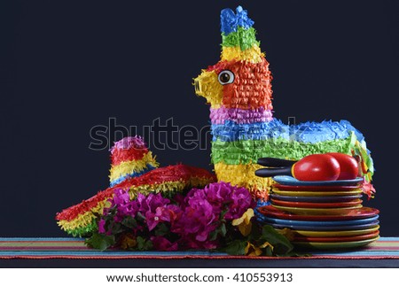 Colorful Happy Cinco de Mayo party table with rainbow straw donkey and sombrero pinata against a black background.