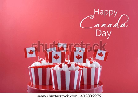 Happy Canada Day Party Cupcakes on a red cake stand with maple leaf flags on a white wood table and red background.