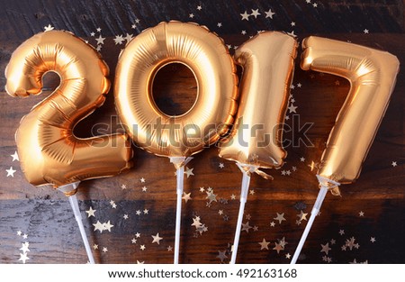 Happy 2017 gold New Year Balloons with glitter stars on dark wood table background.